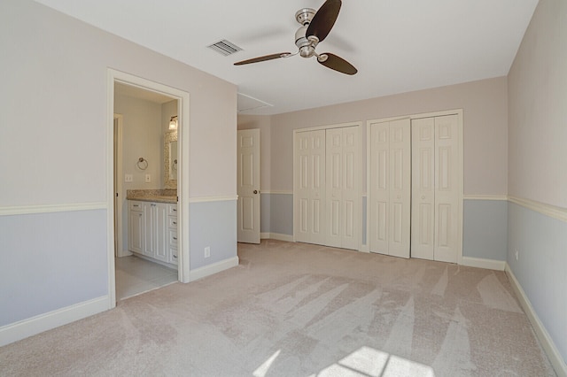 unfurnished bedroom with ceiling fan, ensuite bathroom, light carpet, and multiple closets