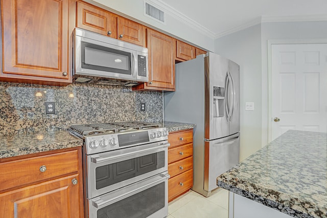 kitchen with dark stone countertops, decorative backsplash, light tile patterned flooring, appliances with stainless steel finishes, and ornamental molding