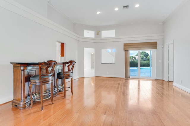 interior space with bar area, light hardwood / wood-style flooring, crown molding, and a towering ceiling