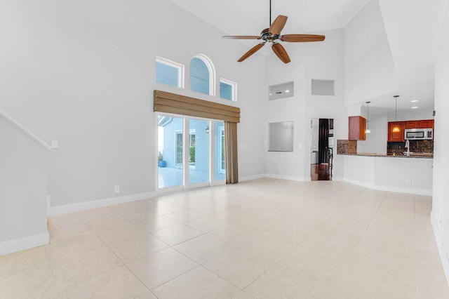 unfurnished living room featuring ceiling fan, light tile patterned floors, and a high ceiling