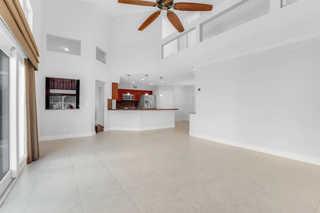 unfurnished living room with ceiling fan, a towering ceiling, a wealth of natural light, and light tile patterned flooring