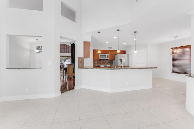 kitchen with light tile patterned floors, appliances with stainless steel finishes, stone countertops, and hanging light fixtures