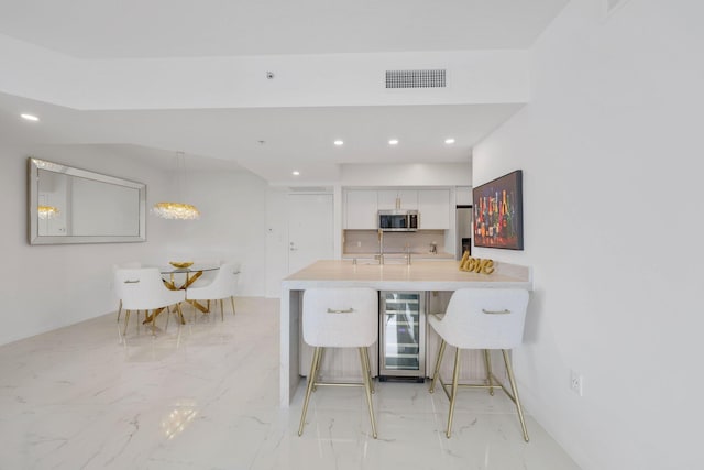 kitchen with white cabinetry, stainless steel appliances, wine cooler, kitchen peninsula, and a breakfast bar