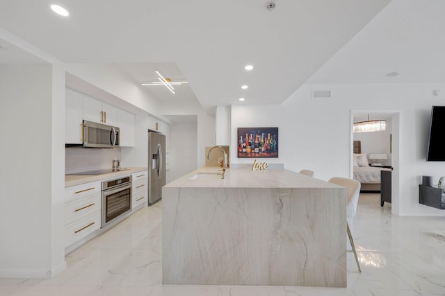 kitchen featuring a breakfast bar, stainless steel appliances, sink, white cabinetry, and an island with sink