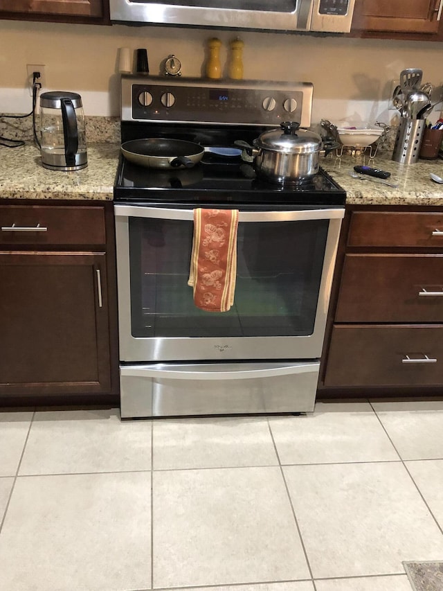 kitchen with light tile patterned floors, electric range, light stone counters, and dark brown cabinetry