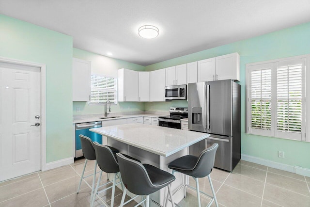 kitchen featuring appliances with stainless steel finishes, sink, light tile patterned floors, white cabinets, and a center island