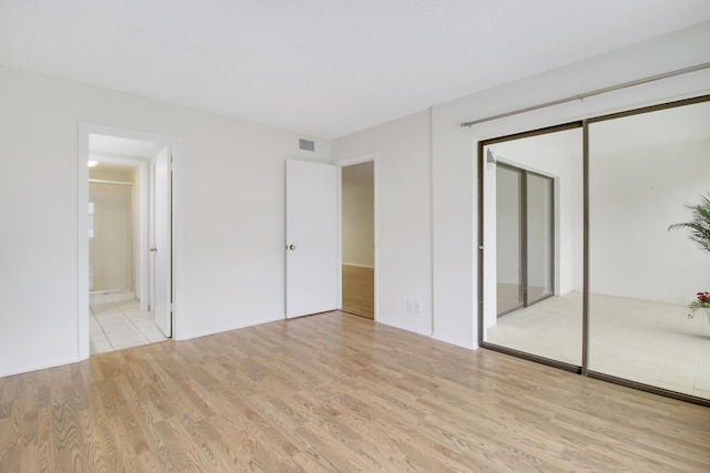 unfurnished bedroom with a closet, light hardwood / wood-style floors, and ensuite bath