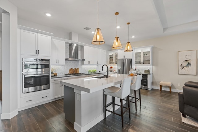 kitchen with sink, wall chimney range hood, decorative light fixtures, a center island with sink, and appliances with stainless steel finishes