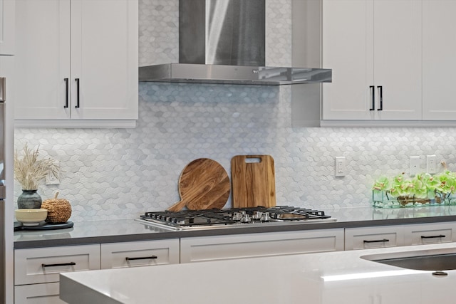 kitchen featuring stainless steel gas stovetop, white cabinetry, wall chimney range hood, and backsplash