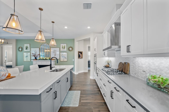 kitchen featuring a kitchen island with sink, sink, decorative light fixtures, and wall chimney range hood