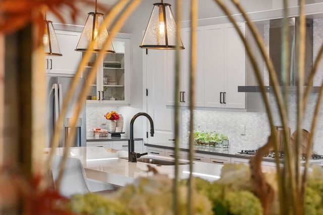 details featuring stainless steel gas stovetop, backsplash, white cabinets, sink, and decorative light fixtures