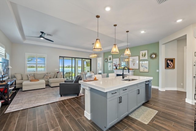 kitchen with stainless steel dishwasher, ceiling fan, a kitchen island with sink, sink, and hanging light fixtures