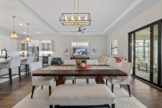 dining area featuring ceiling fan with notable chandelier, a tray ceiling, wine cooler, and sink