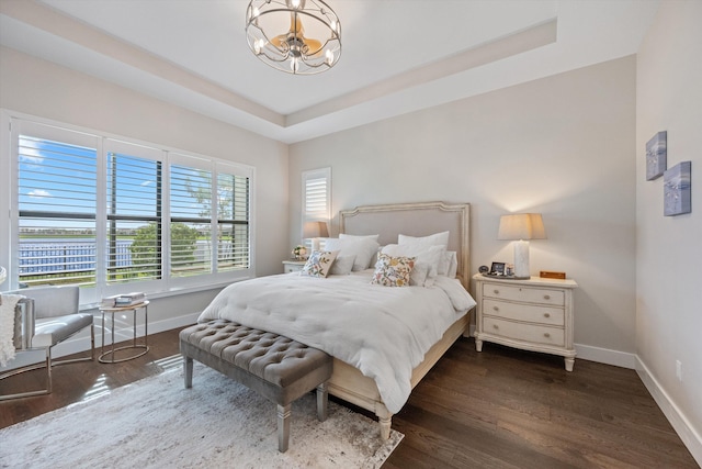 bedroom featuring a raised ceiling, dark wood-type flooring, and a notable chandelier