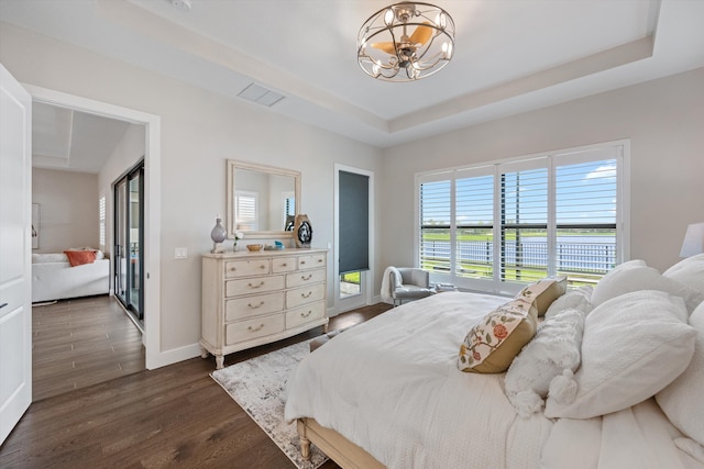 bedroom featuring dark hardwood / wood-style floors, a water view, a chandelier, and a tray ceiling