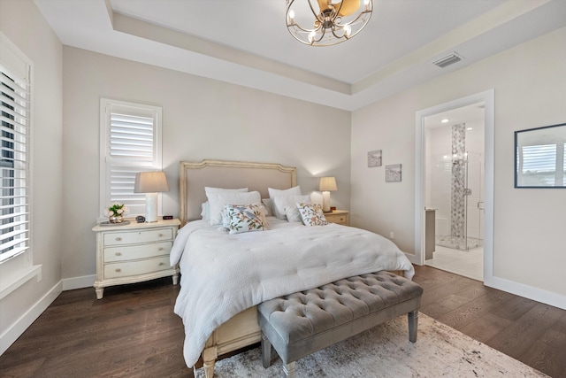 bedroom with multiple windows, dark wood-type flooring, a tray ceiling, and ensuite bath