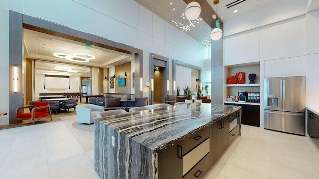 kitchen featuring a center island, dark stone counters, built in shelves, stainless steel fridge, and a towering ceiling