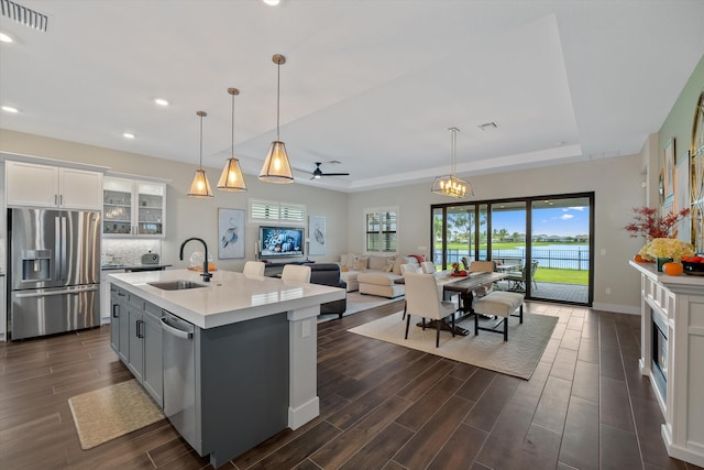 kitchen with sink, an island with sink, a tray ceiling, white cabinets, and appliances with stainless steel finishes