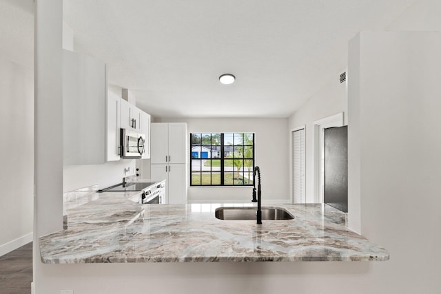 kitchen with kitchen peninsula, light stone counters, stove, and white cabinets