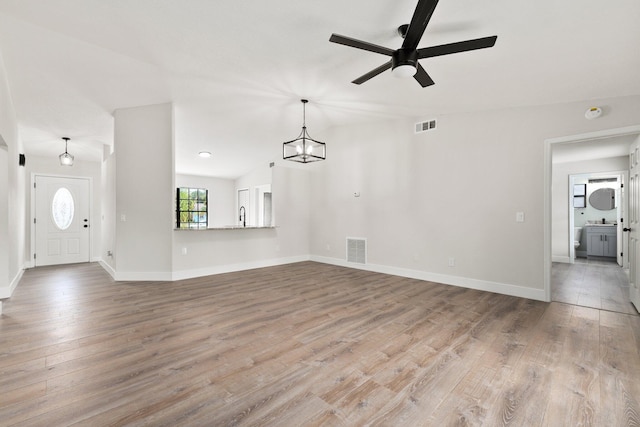 unfurnished living room with sink, ceiling fan with notable chandelier, and light wood-type flooring