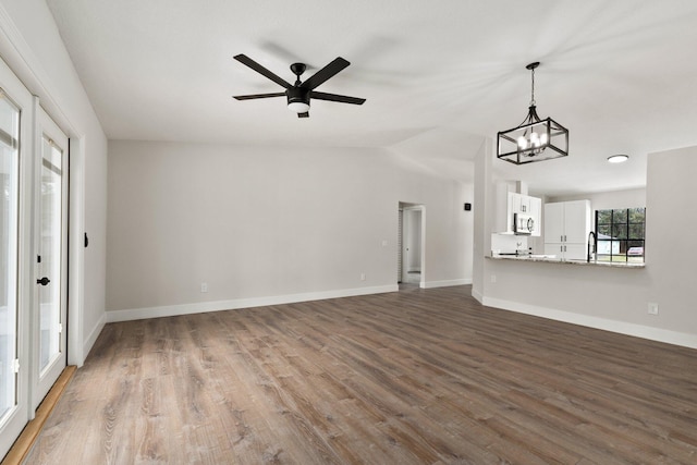 unfurnished living room with ceiling fan with notable chandelier, hardwood / wood-style flooring, lofted ceiling, and sink