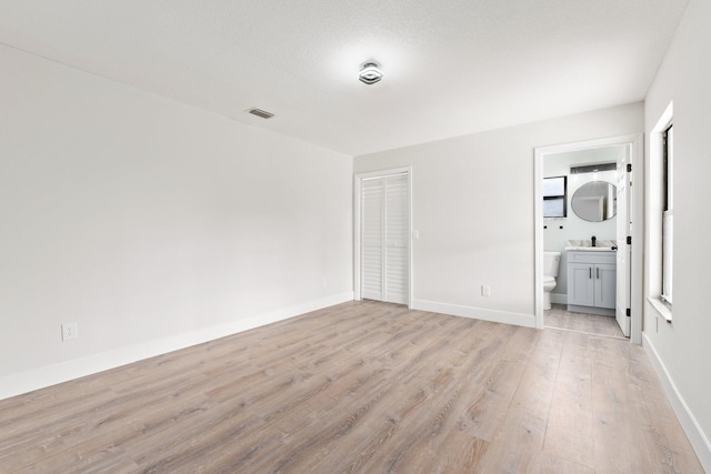 unfurnished bedroom featuring ensuite bathroom, sink, light wood-type flooring, a textured ceiling, and a closet