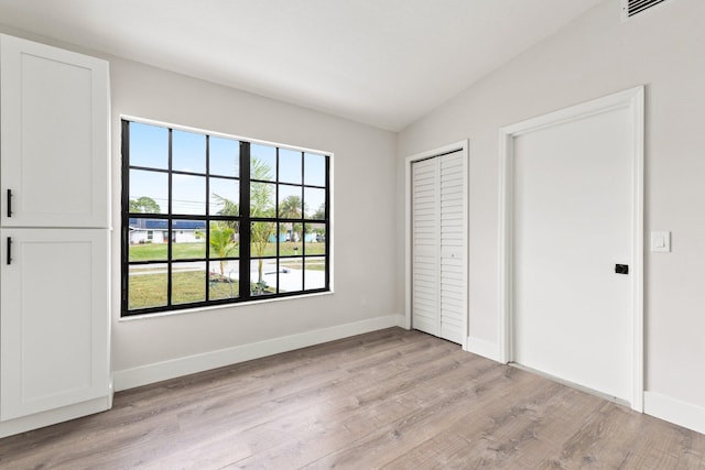 unfurnished bedroom featuring multiple windows, vaulted ceiling, and light wood-type flooring