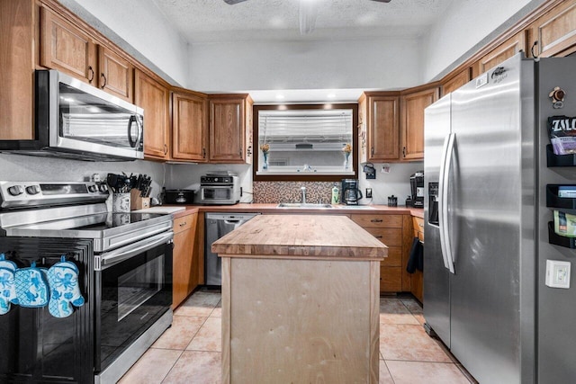 kitchen featuring a center island, sink, stainless steel appliances, a textured ceiling, and light tile patterned flooring