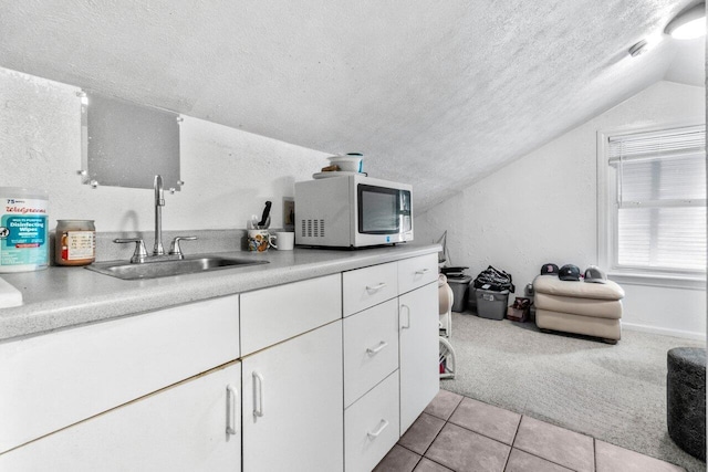 kitchen featuring light carpet, sink, vaulted ceiling, a textured ceiling, and white cabinetry