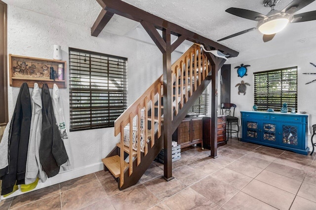 staircase with ceiling fan, beamed ceiling, and a textured ceiling