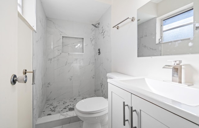 bathroom with a tile shower, toilet, and vanity