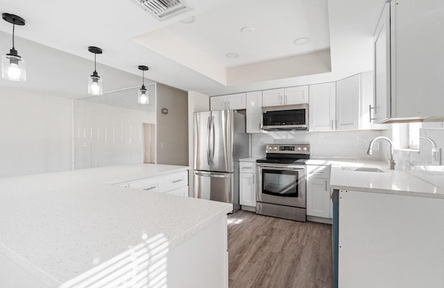 kitchen featuring appliances with stainless steel finishes, white cabinets, sink, kitchen peninsula, and a tray ceiling