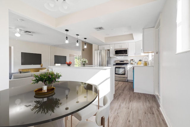 kitchen featuring hanging light fixtures, a raised ceiling, appliances with stainless steel finishes, light wood-type flooring, and white cabinets