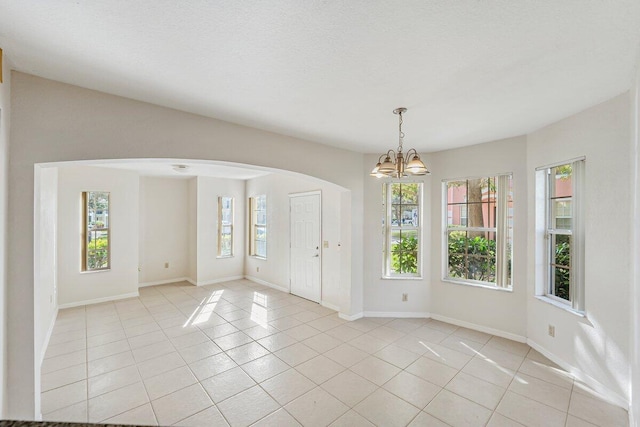 tiled spare room with plenty of natural light and a chandelier