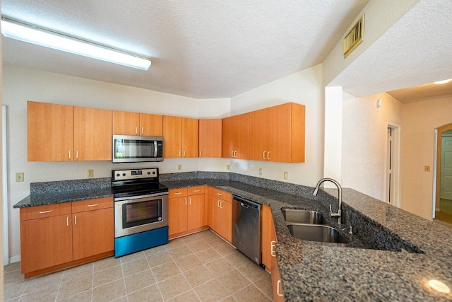 kitchen with a textured ceiling, stainless steel appliances, dark stone counters, and sink