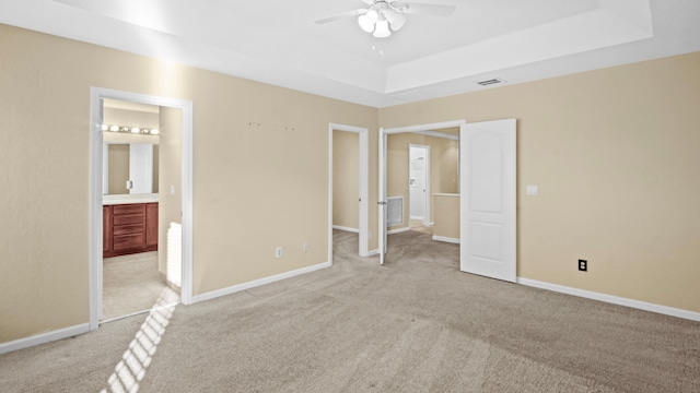 unfurnished bedroom with ceiling fan, ensuite bath, a tray ceiling, and light carpet