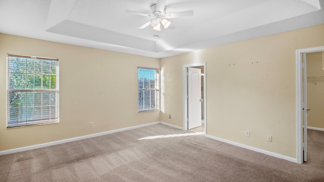 unfurnished bedroom featuring multiple windows, a walk in closet, a raised ceiling, and ceiling fan