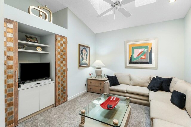 living room with ceiling fan, built in features, lofted ceiling with skylight, and light carpet