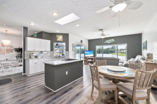 kitchen featuring dark wood-type flooring, a skylight, tasteful backsplash, decorative light fixtures, and white cabinetry