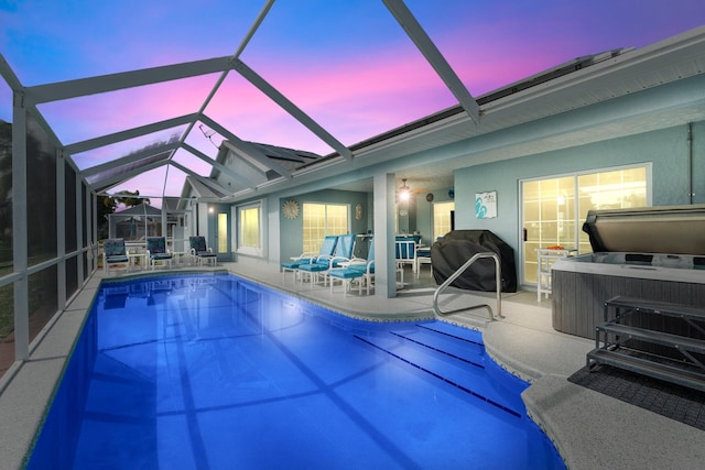 pool at dusk featuring glass enclosure, a patio, and a hot tub