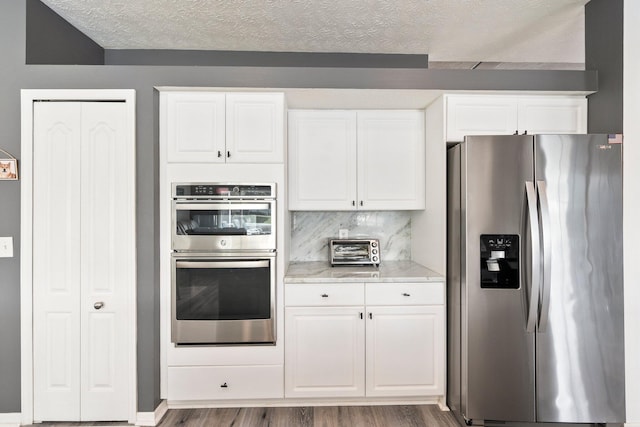 kitchen featuring backsplash, dark wood-type flooring, a textured ceiling, appliances with stainless steel finishes, and white cabinetry