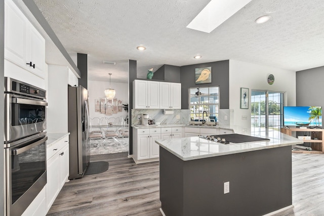 kitchen featuring kitchen peninsula, decorative backsplash, a skylight, stainless steel appliances, and white cabinetry