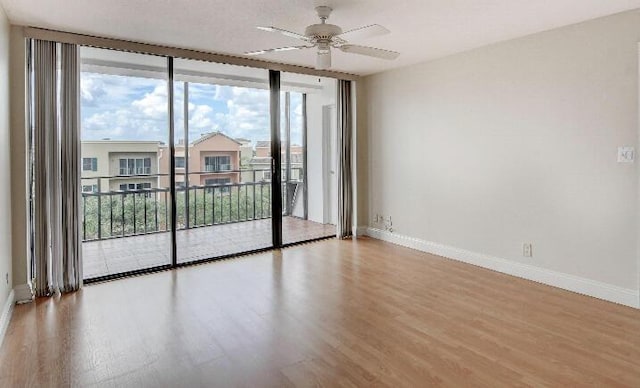 spare room featuring ceiling fan, wood-type flooring, and a wall of windows