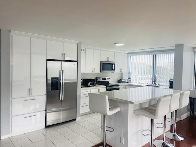 kitchen with a breakfast bar, white cabinets, stainless steel appliances, and light tile patterned floors