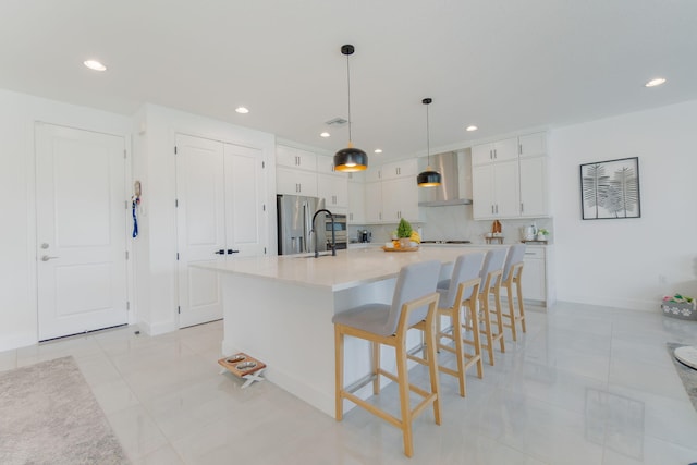 kitchen with white cabinetry, wall chimney range hood, stainless steel fridge, a spacious island, and decorative light fixtures