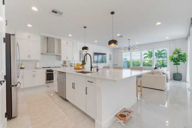 kitchen featuring wall chimney exhaust hood, stainless steel appliances, a kitchen island with sink, sink, and white cabinetry