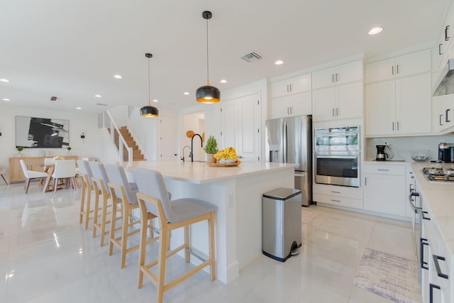 kitchen featuring stainless steel appliances, pendant lighting, a breakfast bar area, a kitchen island with sink, and white cabinets