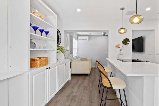 kitchen featuring a kitchen breakfast bar, a wall unit AC, kitchen peninsula, decorative light fixtures, and white cabinets