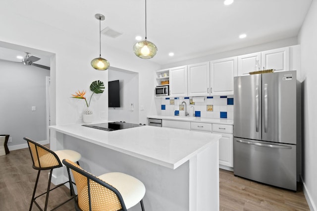 kitchen with kitchen peninsula, decorative backsplash, a breakfast bar, stainless steel appliances, and white cabinetry