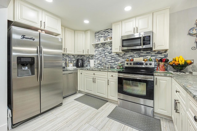 kitchen with light stone countertops, appliances with stainless steel finishes, backsplash, sink, and white cabinetry